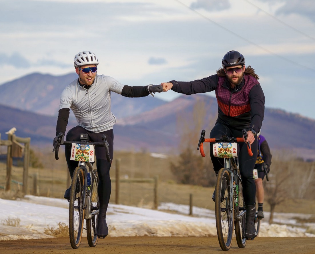 A group of cyclists riding a gravel road beside snowy fields