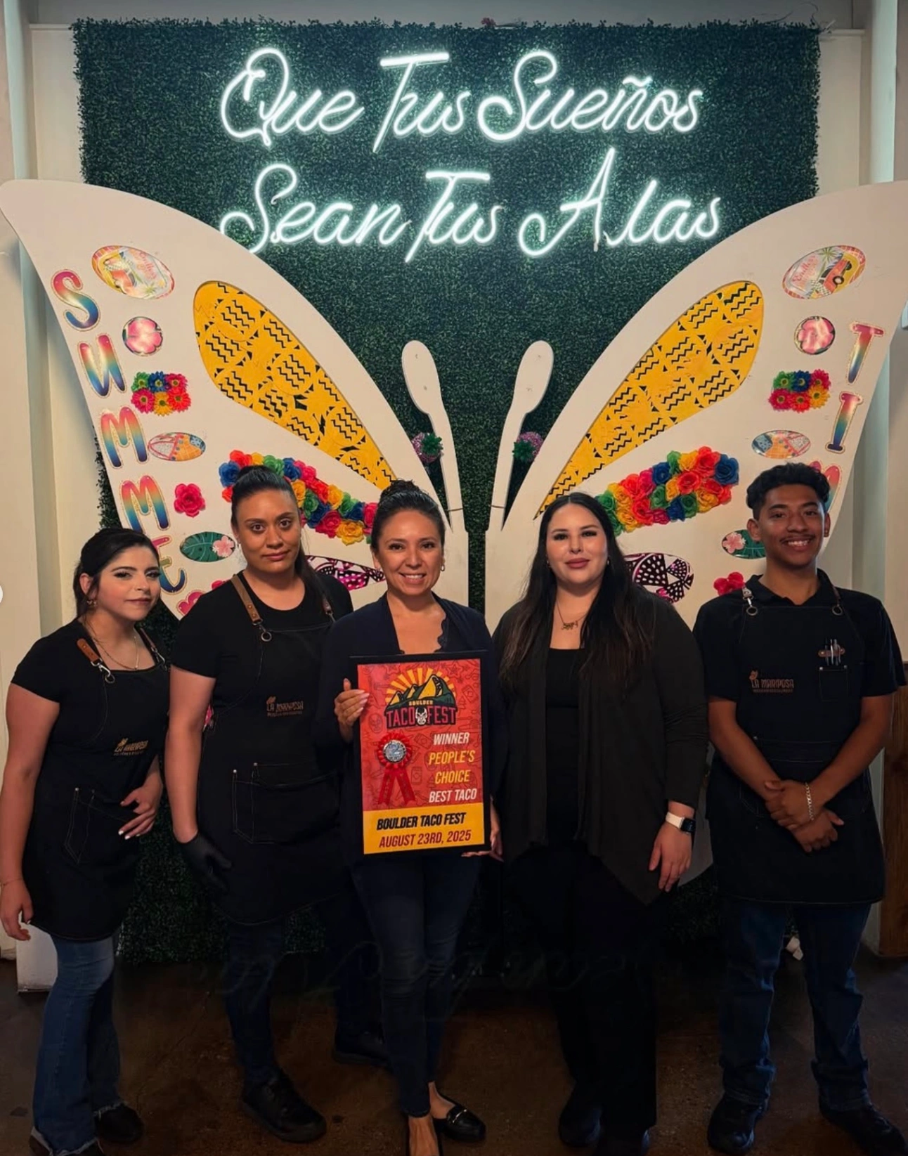 Group holding a Boulder Taco Fest People's Choice Best Taco winner sign in front of a butterfly wing backdrop